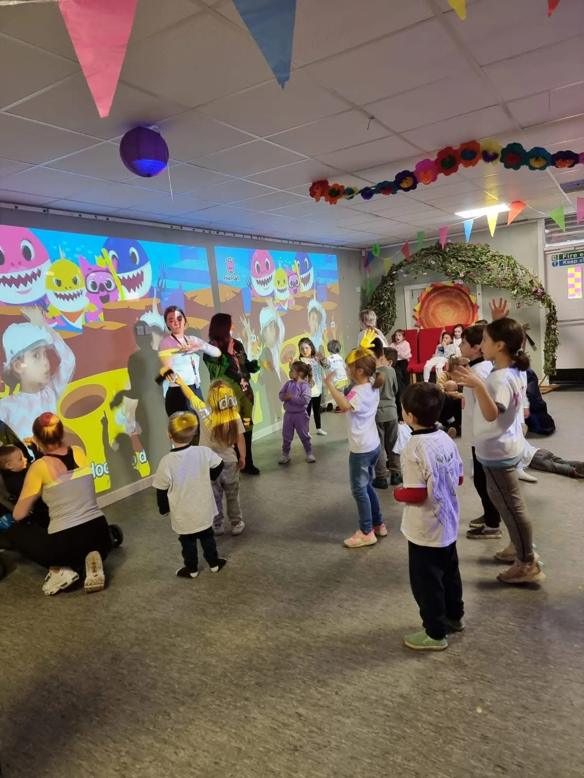 Children dancing and playing in an indoor space decorated with colourful bunting and a large animated projection on the wall.