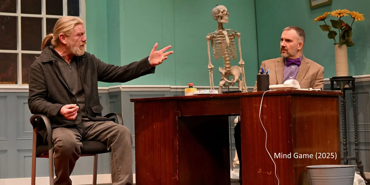 Two men in conversation at a desk in a classroom setting with a skeleton model behind them.