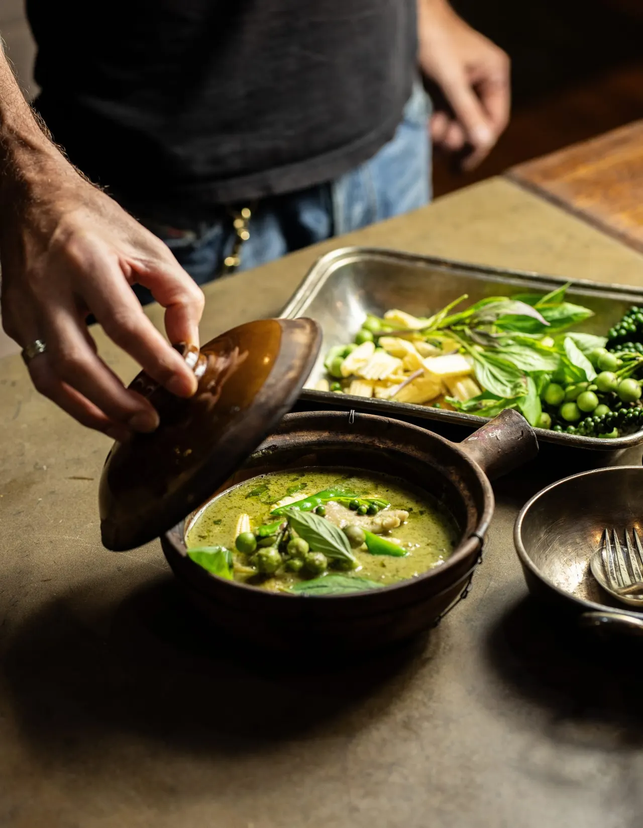 Person pouring green herb sauce from a jug over a dish of vegetables and seafood at a dining table.