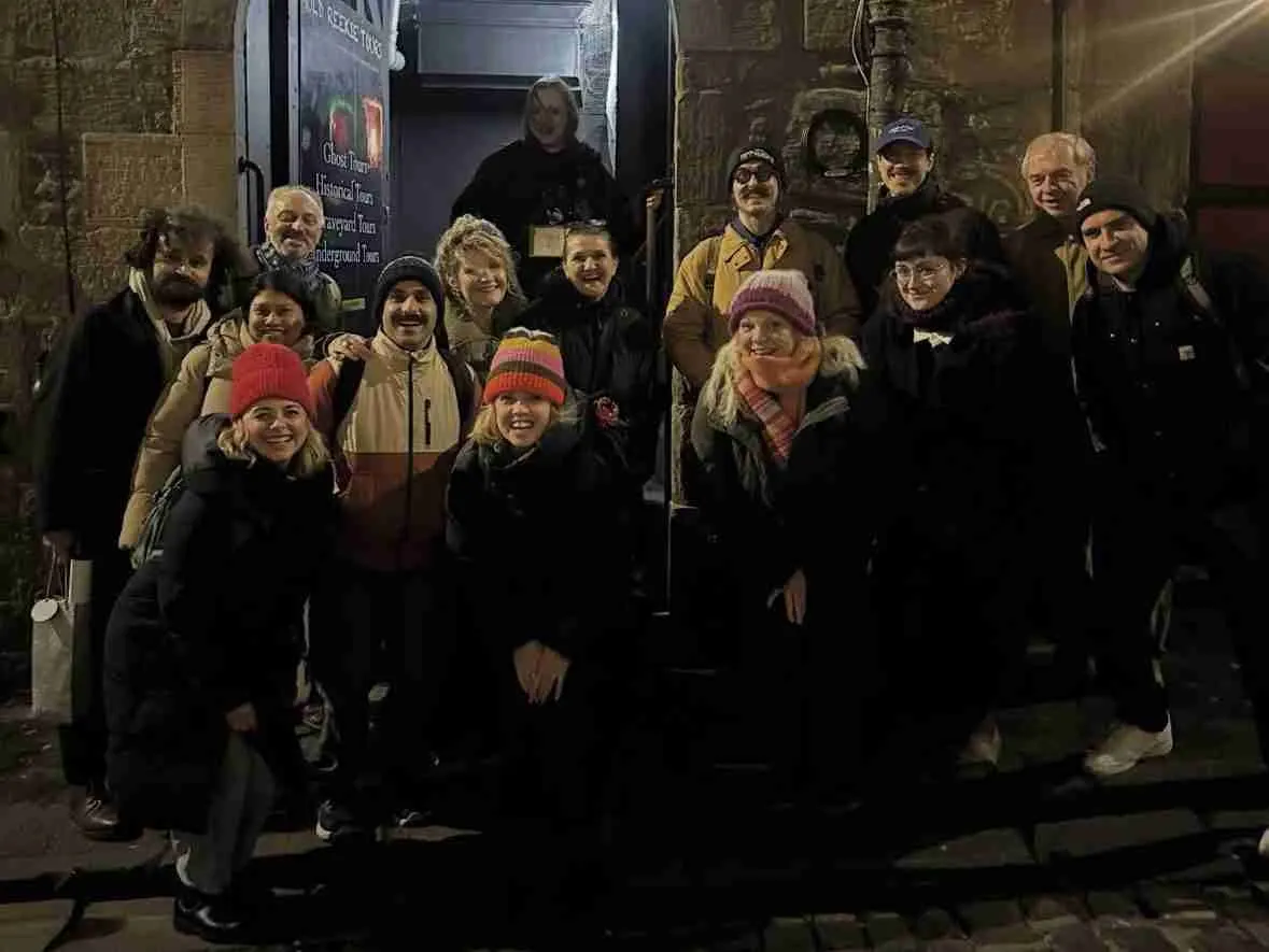A group of tourists gathered at night outside an underground tour entrance, smiling at the camera.