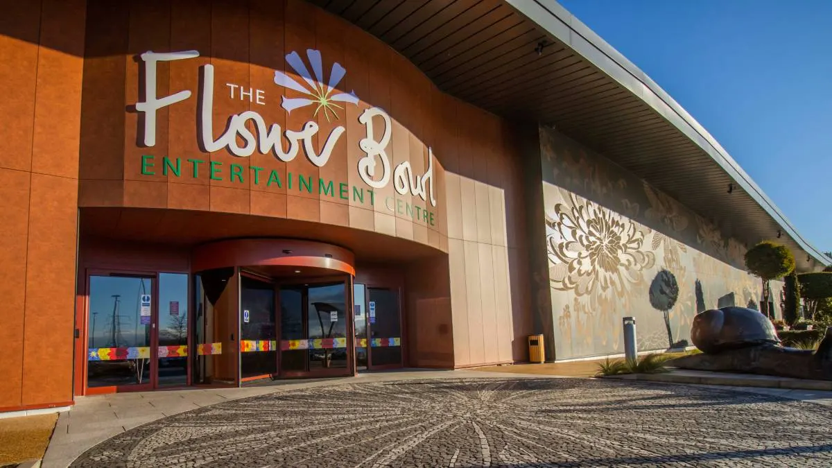Modern entertainment centre building with orange cladding, large signage, and patterned courtyard on a sunny day.
