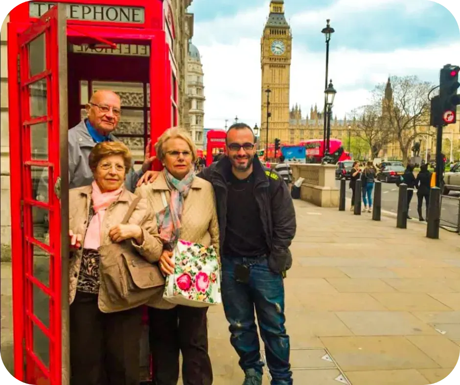 Four people posing by a red telephone box with Big Ben and the Houses of Parliament in the background in London.
