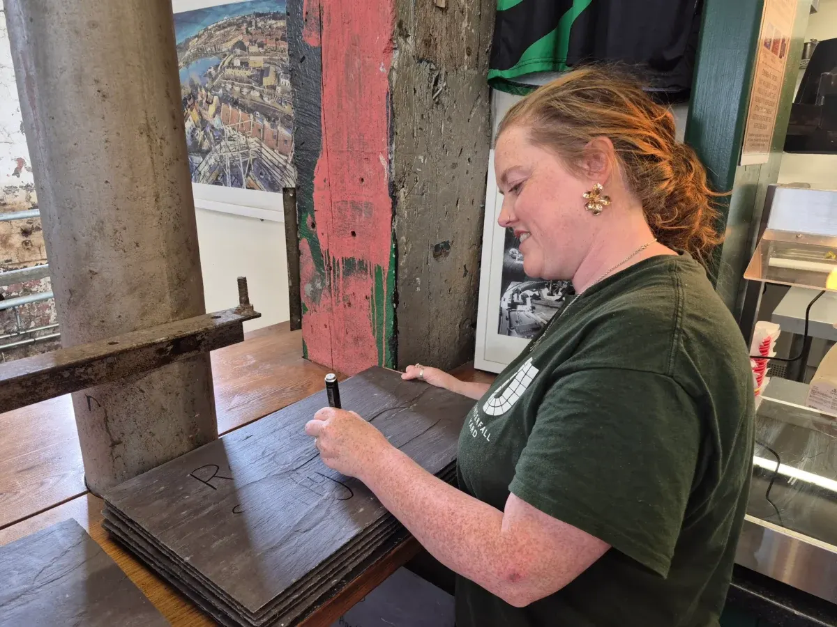 Woman in green shirt examining a historic wooden door or gate panel inside a museum or heritage venue display area.