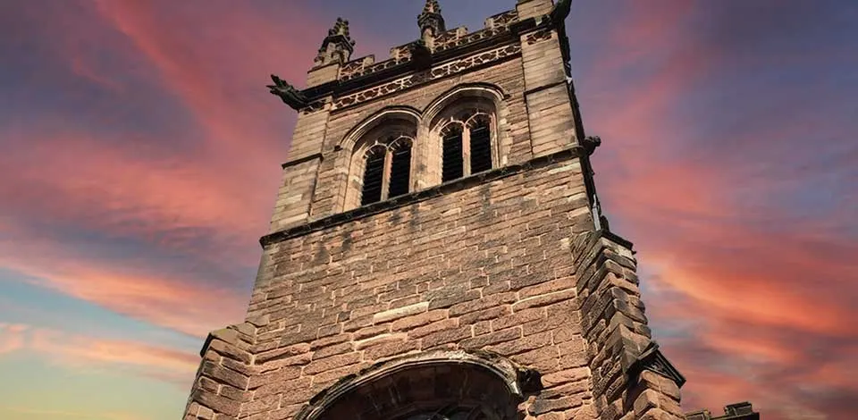 Stone church tower with ornate crenellations and arched windows against a dramatic pink and purple sunset sky.