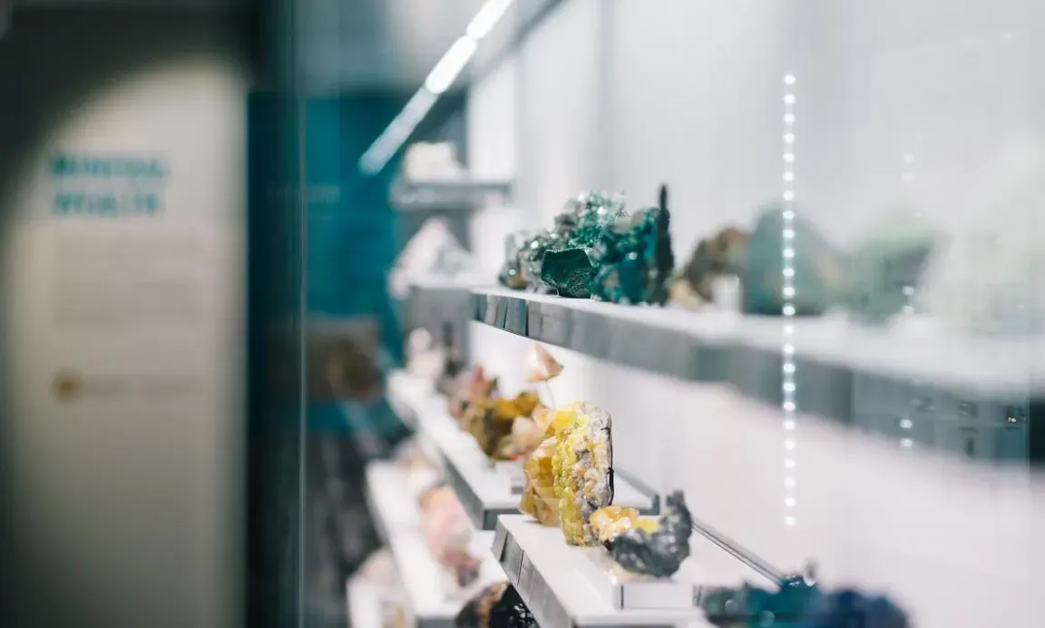 Mineral and crystal specimens displayed on white shelving behind glass in a museum exhibition.