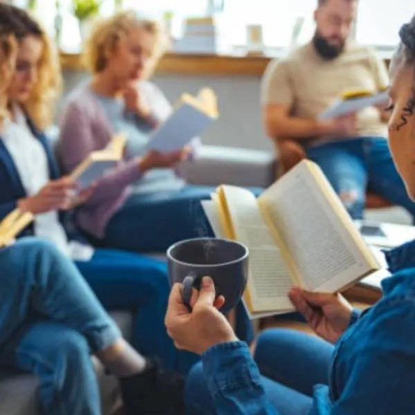 Group of adults sitting together holding open books and cups during a reading or discussion session indoors.