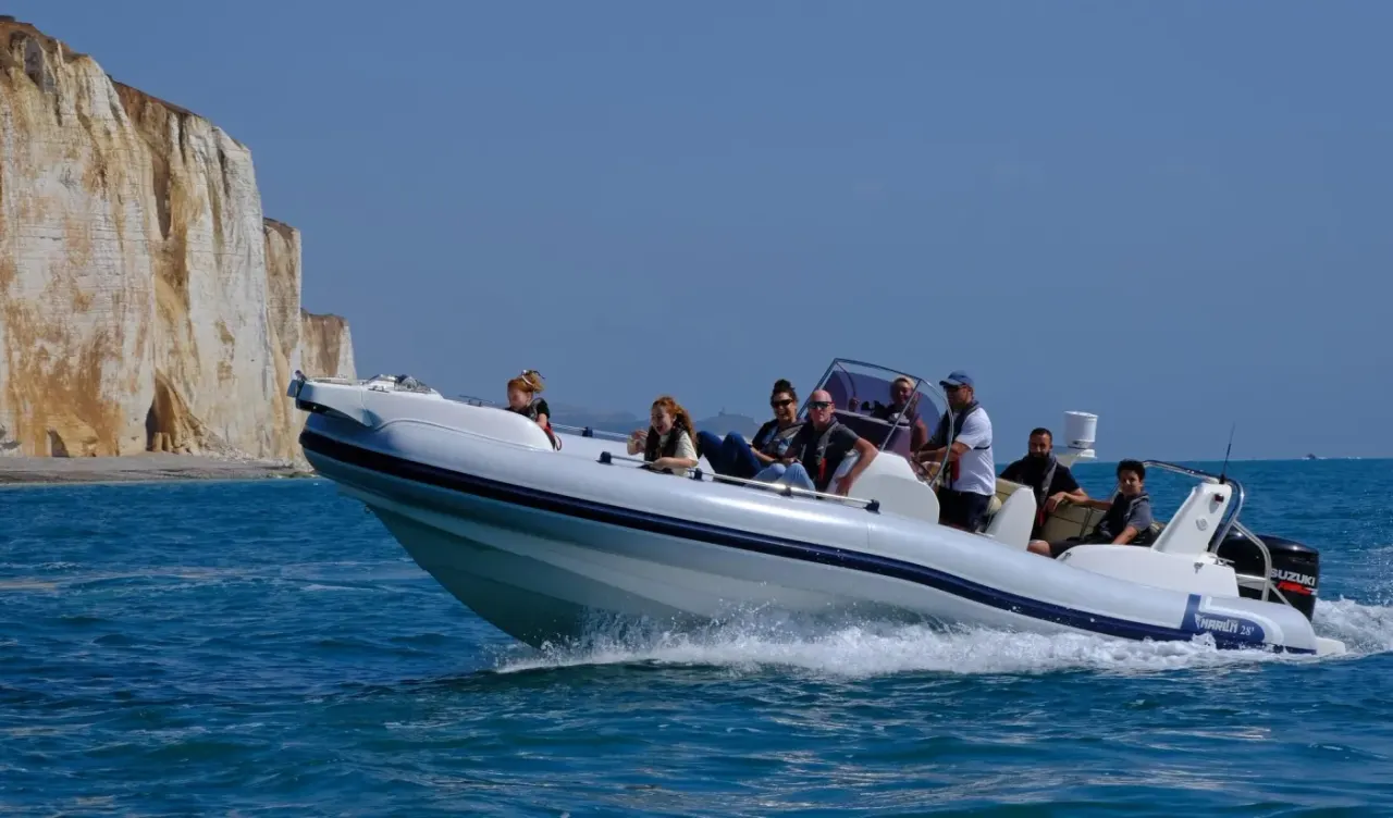 A speedboat full of passengers approaches white chalk cliffs on a sunny day at sea.