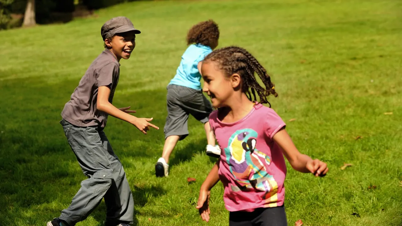 Three children running and playing together on a sunny, open grass field.