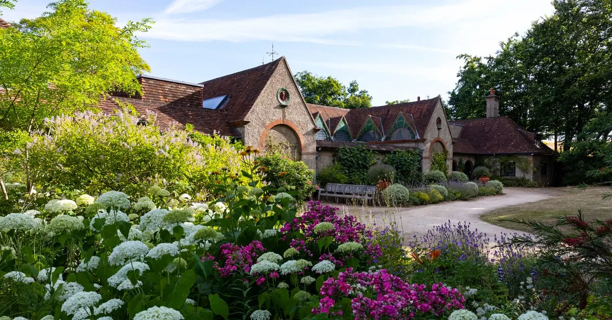 A brick and stone building with arched windows surrounded by flowering gardens featuring white and magenta blooms and lavender plants.