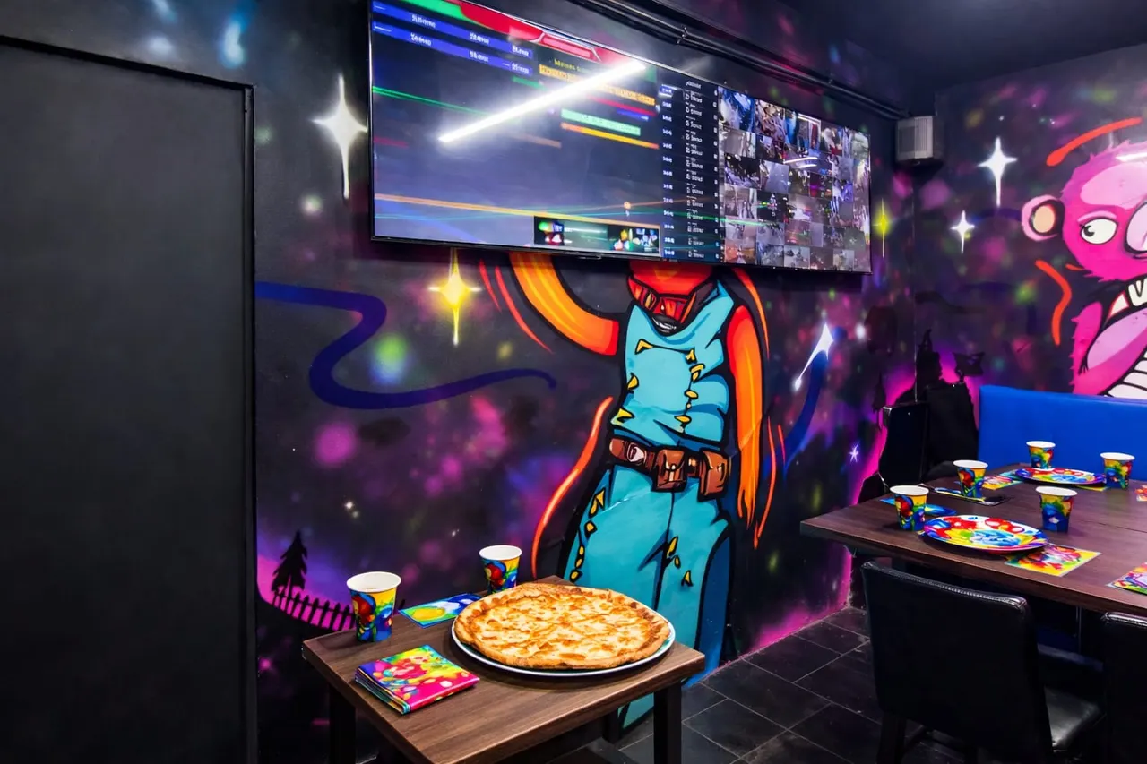 Gaming arcade with pizza and drinks on tables beneath neon murals and screens displaying game content.