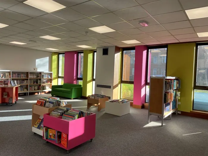 Bright modern library interior with colourful shelving units, books on display, and a green seating area.