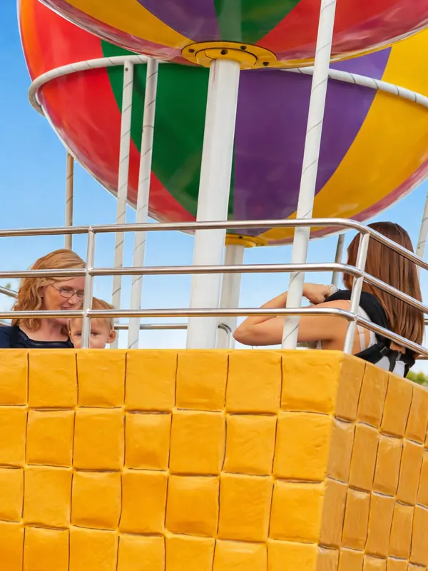 Two children in a colourful hot air balloon basket against a blue sky.