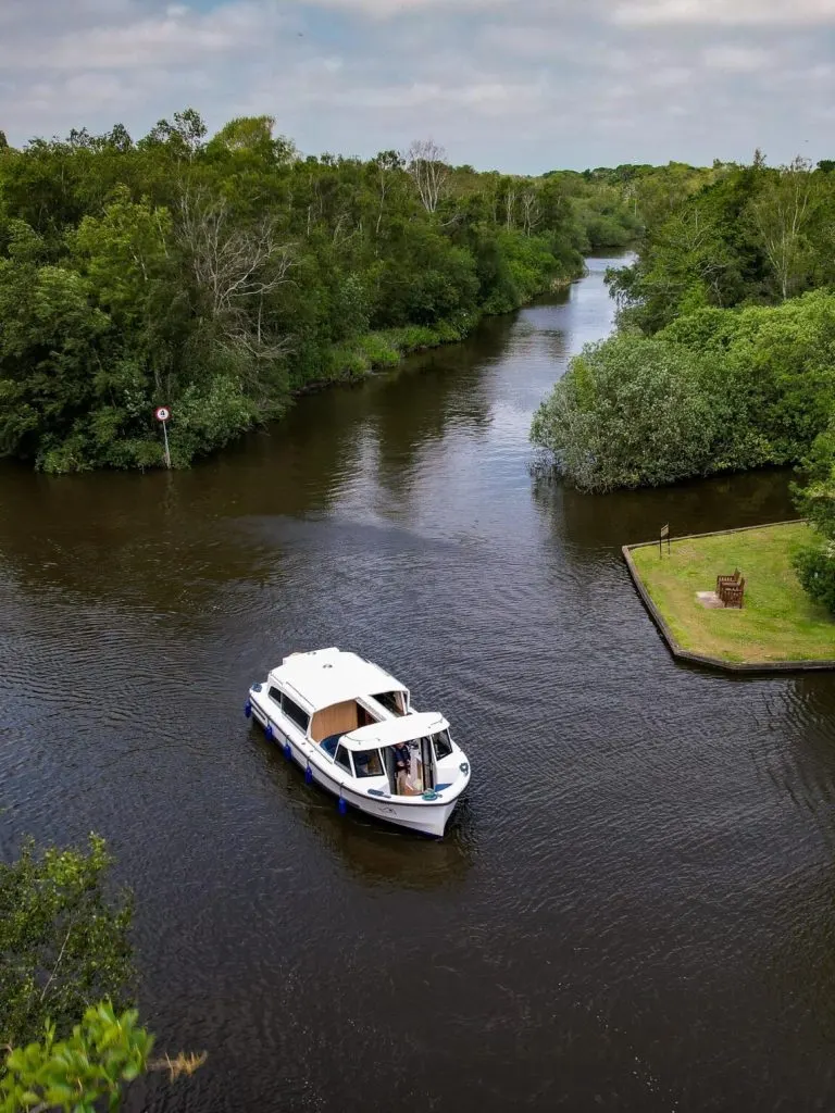 White and blue motorboat moored on a river surrounded by woodland and green banks.