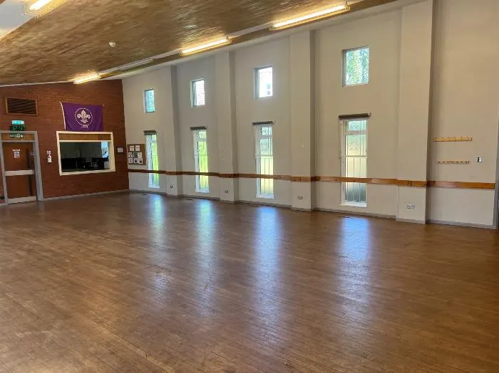 Empty dance or activity studio with wooden floor, mirrored wall and tall windows.