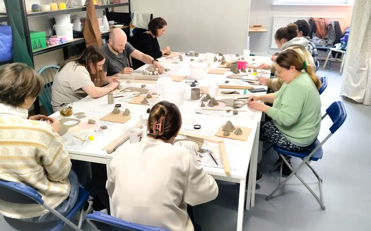 Group of adults seated around a table working on a pottery or clay-making workshop.