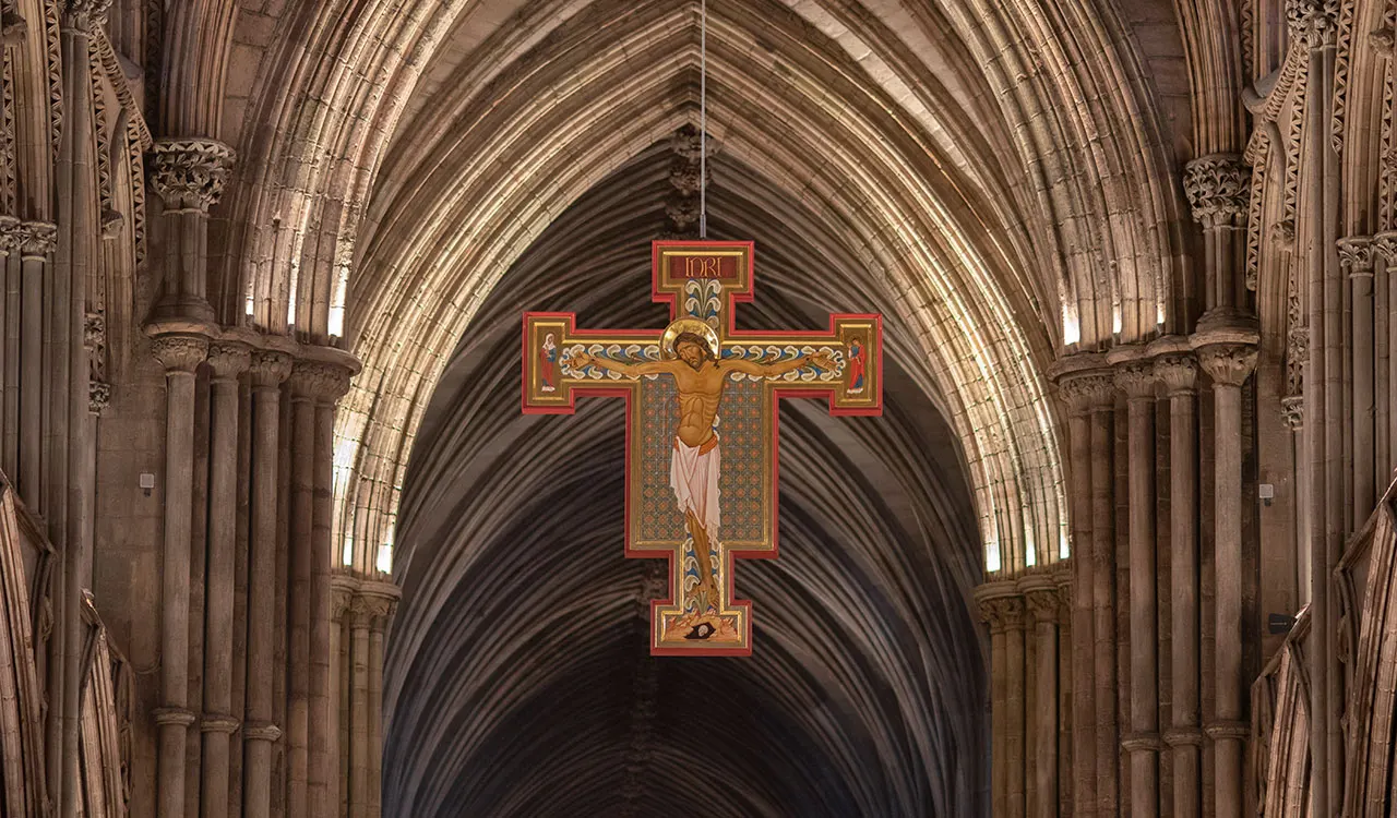 Ornate Gothic cathedral interior with ribbed vaulting stretching into the distance and a large decorated crucifix suspended in the nave.