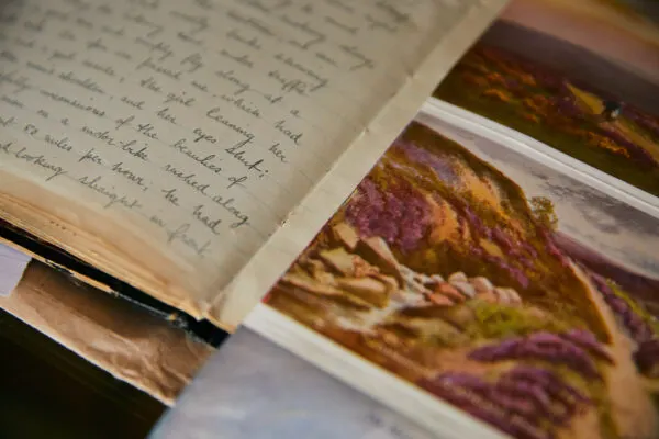 Open handwritten journal next to photographs of purple heather-covered moorland landscape.