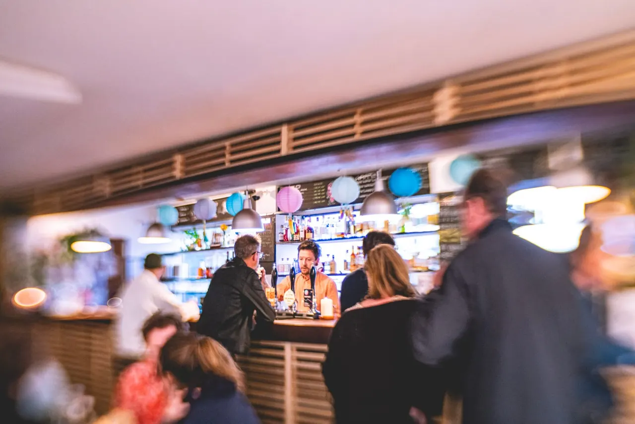 Customers at a busy bar counter with a bartender serving drinks, colourful lanterns hanging above.