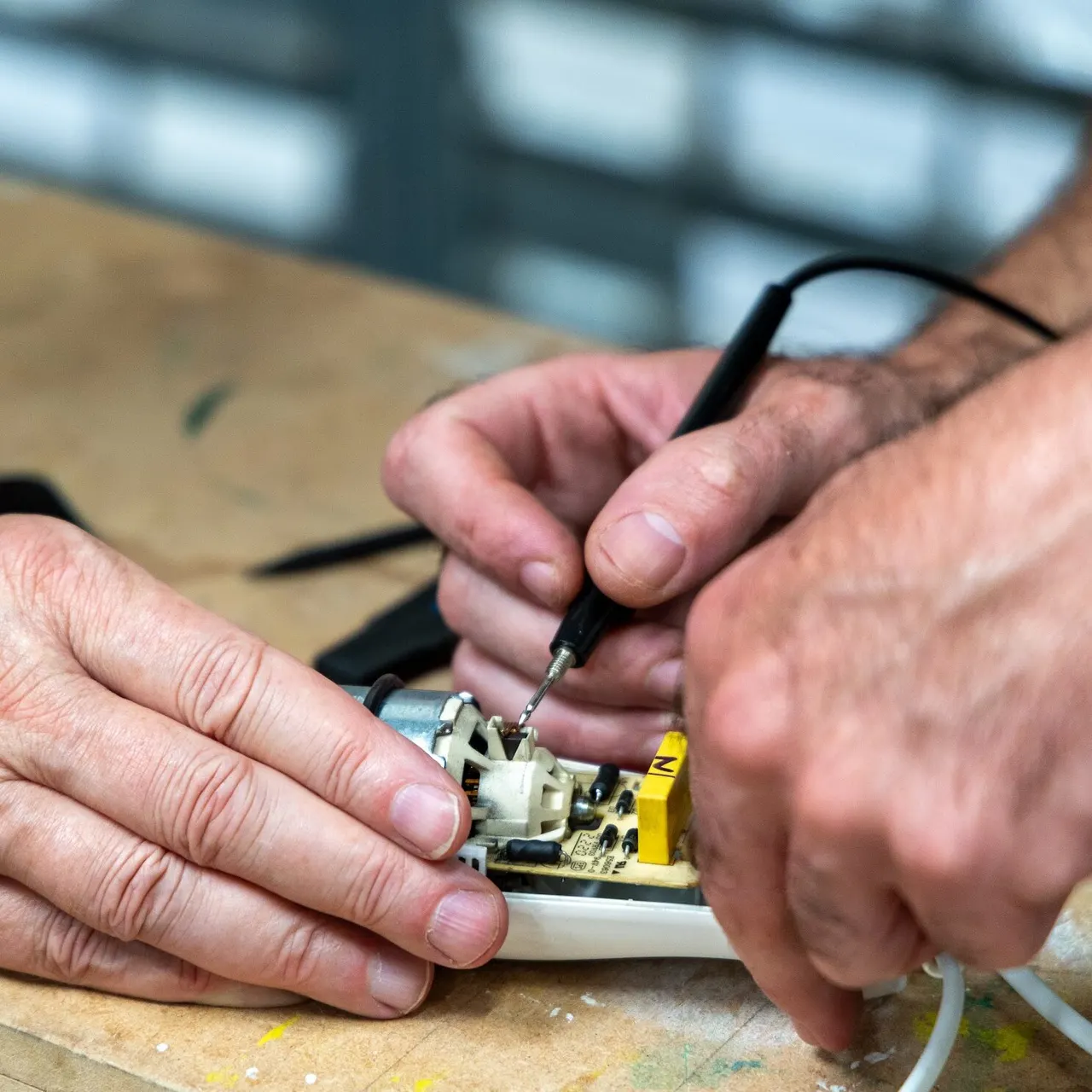 Person soldering an electronic circuit board component with a soldering iron.