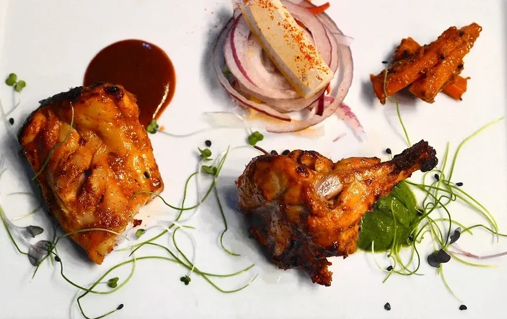 Glazed roasted poultry portions with red onion, microgreens and sauce on a white plate.