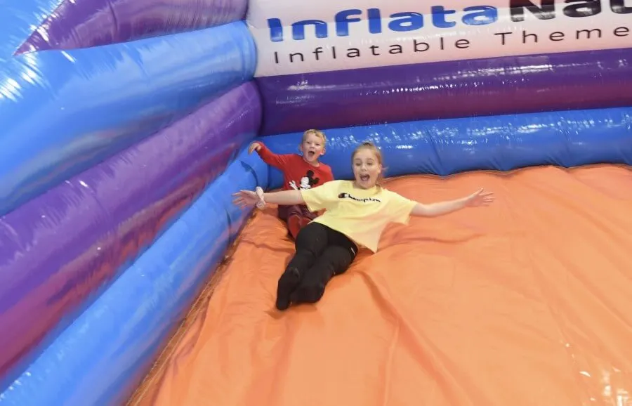 Two children playing and sliding on a large inflatable bouncy castle attraction.