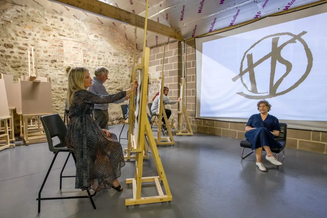 Adults participate in an interactive art workshop with easels and canvases in a stone-walled studio space.