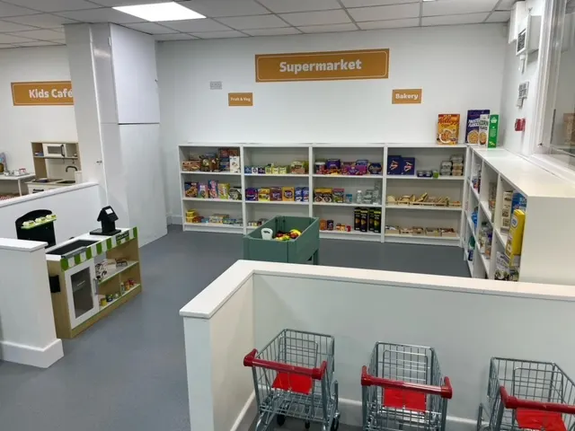 An indoor play area's pretend supermarket with shelving stocked with toy food items, shopping trolleys, and a kids' café area.