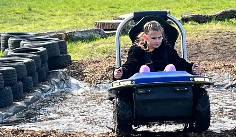 Child in a go-kart on a track with tyres lining the course at an outdoor leisure venue.