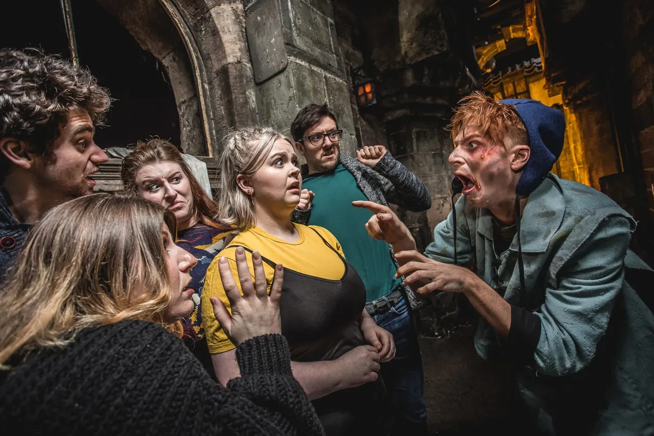 A group of six people react with shock and fear inside a dimly lit stone dungeon setting at night.