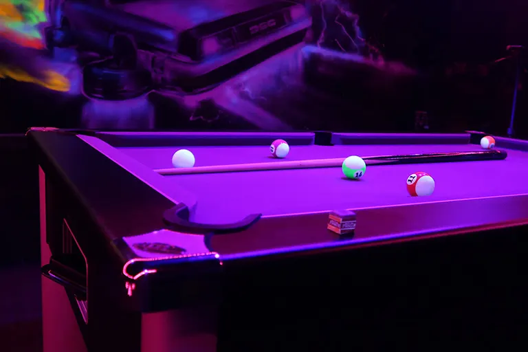 Pool table with neon lighting and illuminated balls under purple and pink neon lights.