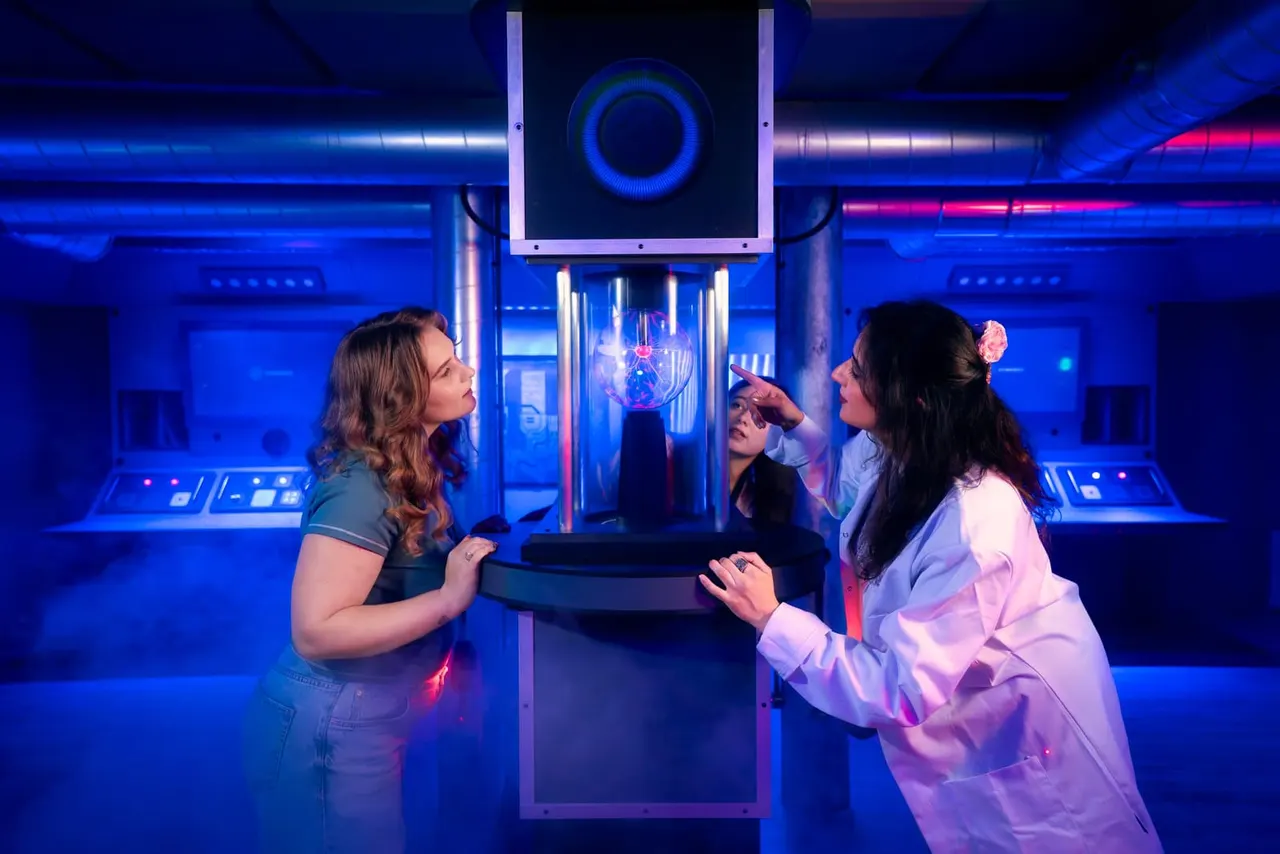 Four visitors interact with an illuminated plasma ball display in a blue-lit science or technology exhibition space.