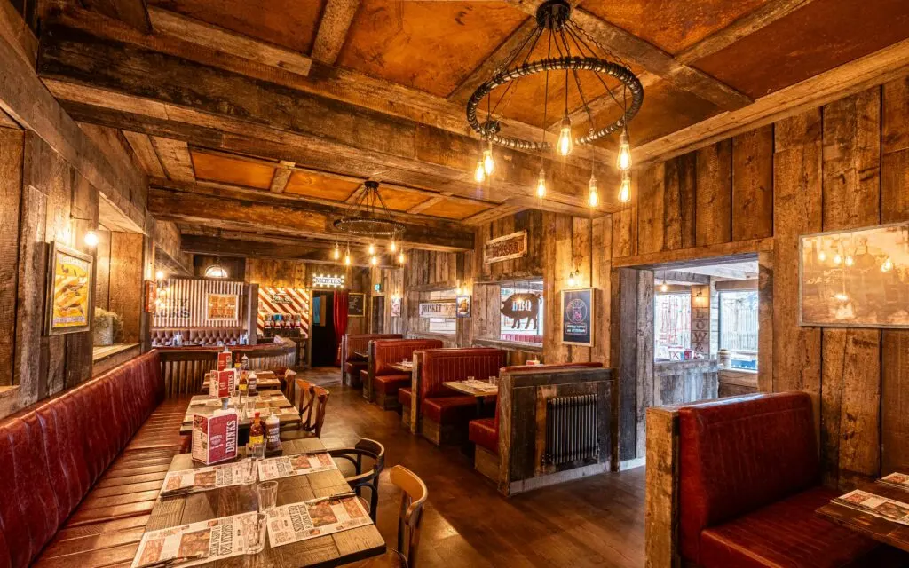 Interior of a rustic steakhouse with wooden beams, red booths, and vintage décor with hanging lights.