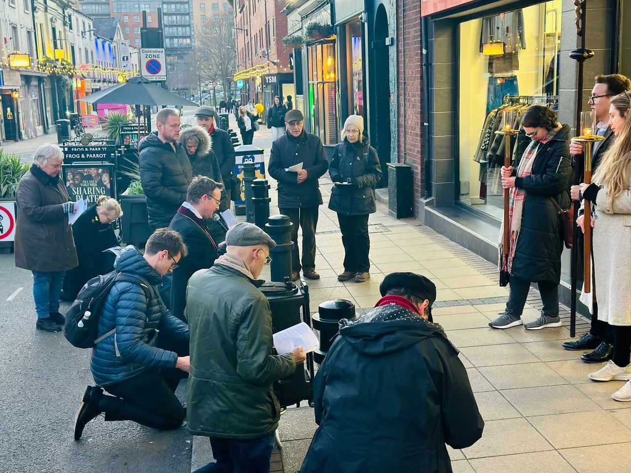 A group of people gathered on a city street outside shops during what appears to be a church or community event.