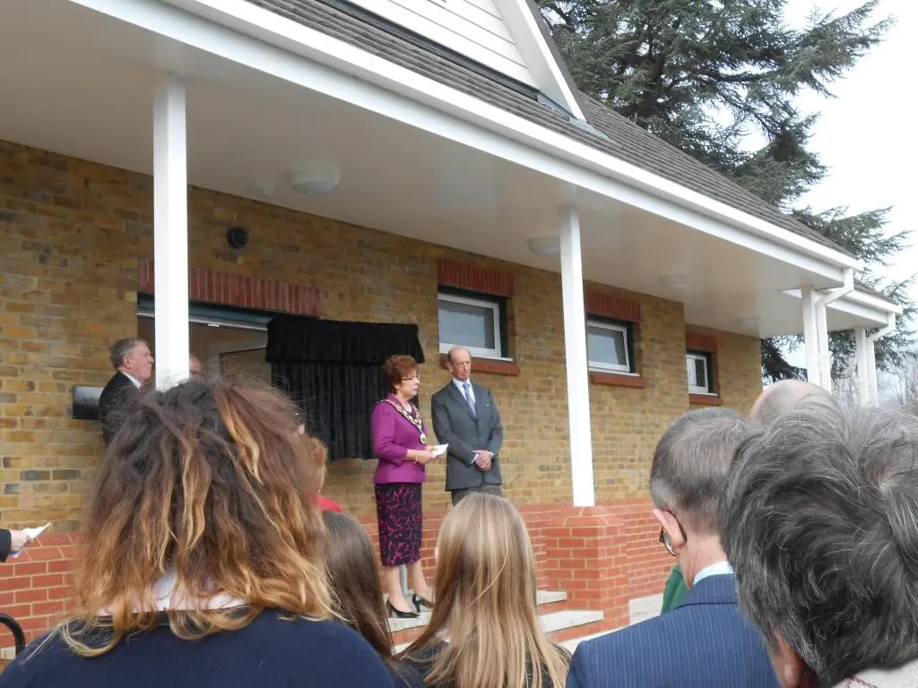 Group of people gathered outside a brick building with white columns for an outdoor event or ceremony.