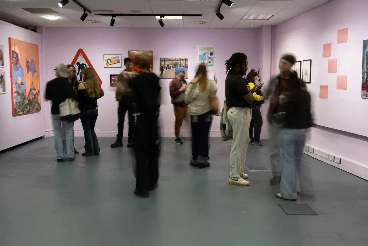 Visitors viewing artwork in a gallery space with lavender walls displaying various framed paintings and prints.