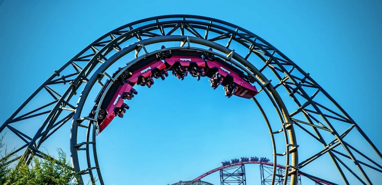 Roller coaster with pink cars carrying riders through a loop against a clear blue sky.