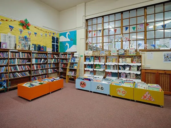 Bright children's library corner with colourful low-level shelving, books and an orange seating bench.