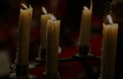 Lit candles with flickering flames arranged on a dark surface against a blurred red background.