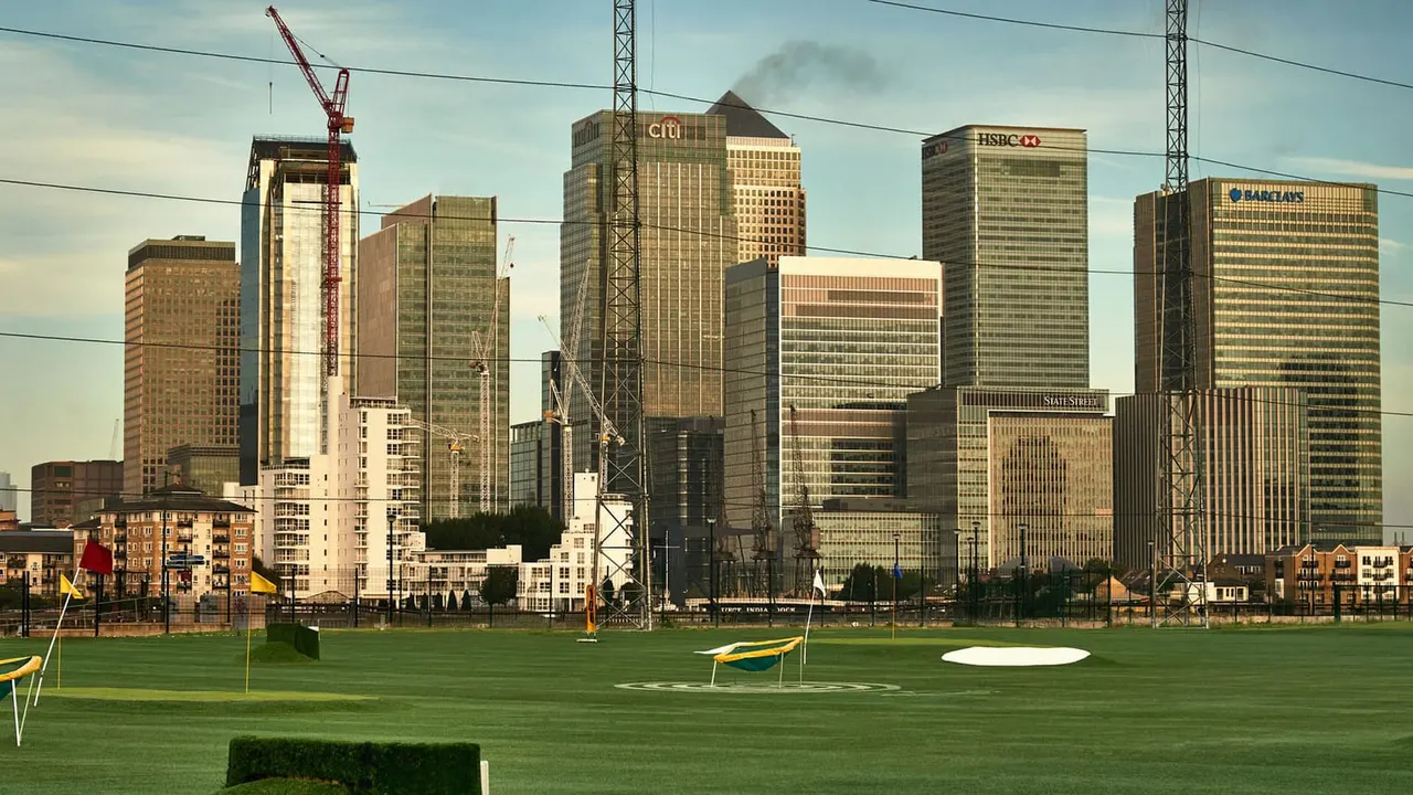 Green putting course with yellow and blue golf equipment, city skyline with high-rise buildings in background.