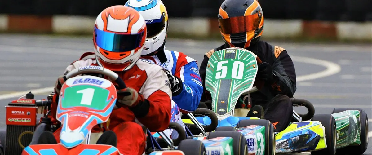 Two kart racers in helmets and racing suits competing on a go-kart track during a race.
