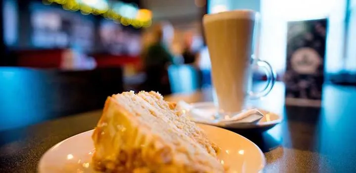 A slice of layered cake on a plate with a glass of beer on a table inside a venue.