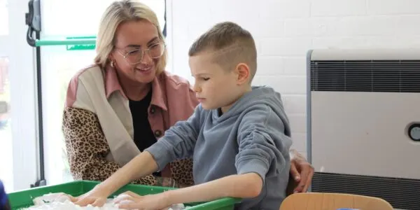 A woman and young boy interact at a touchscreen display during a sensory activity session.