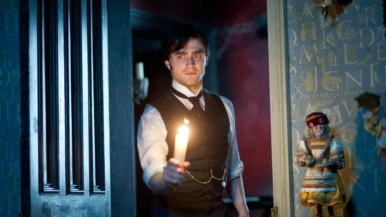 Man in period costume holding a lit candle in a dimly lit corridor with decorative wall panels.