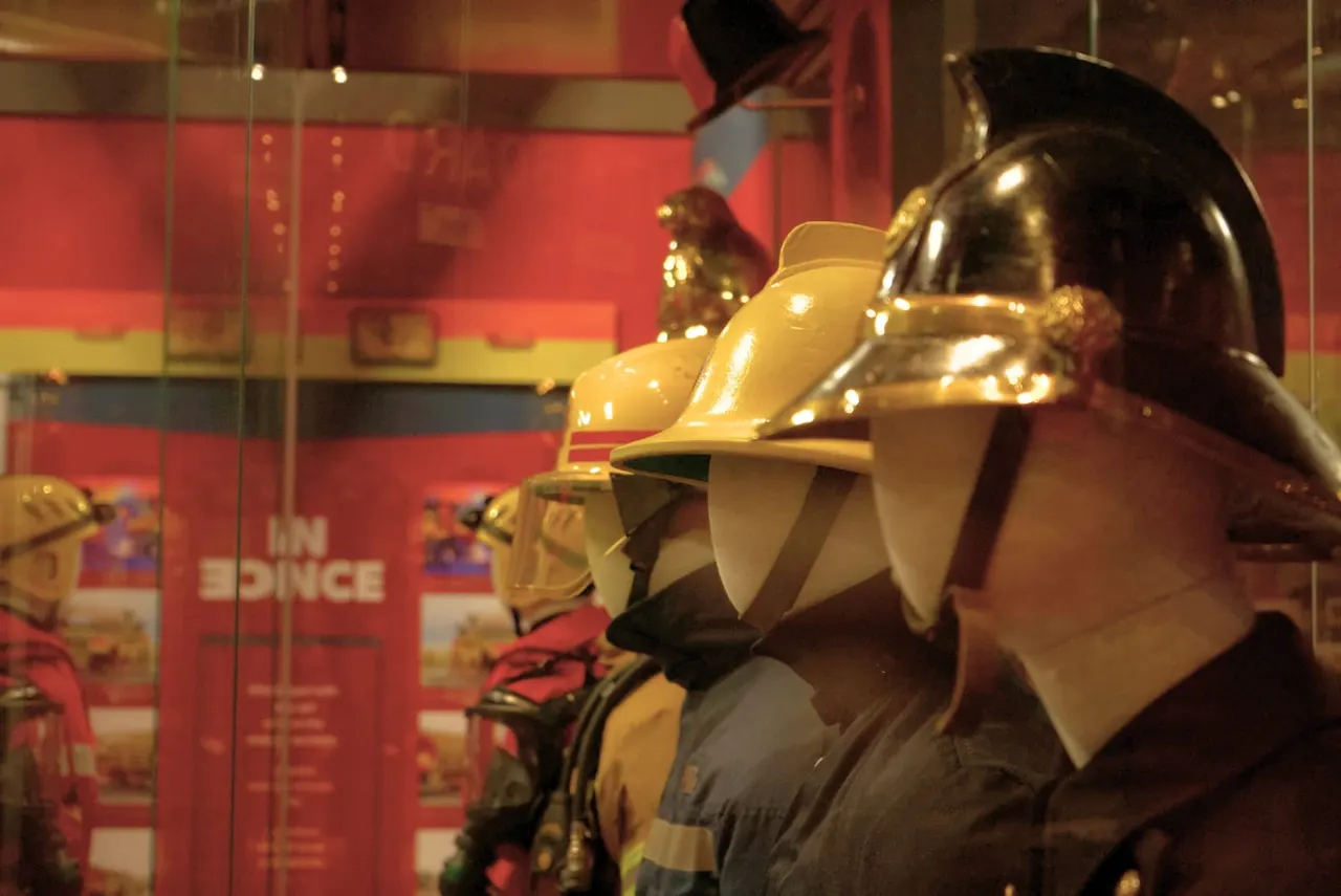 Museum display of vintage firefighting helmets and uniforms with red and gold striped background panels.