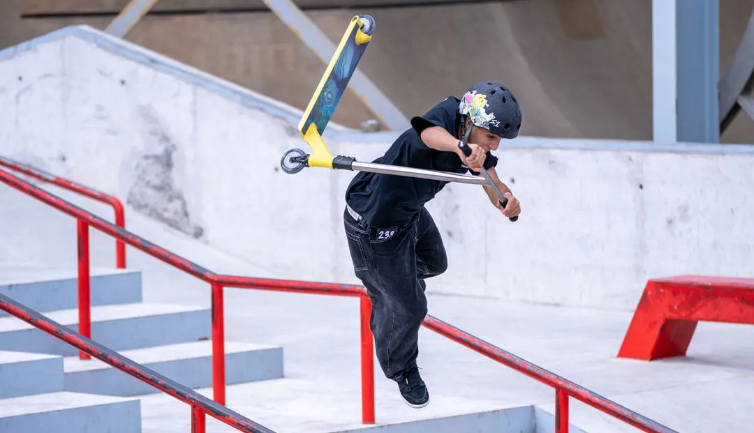 A young skateboarder performs a trick on a rail at an outdoor skate park with concrete features.