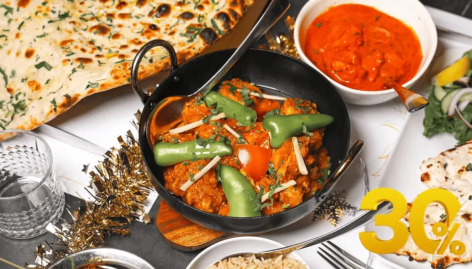 Indian curry dish with peppers and ginger in a black balti bowl, served with naan bread and red sauce.