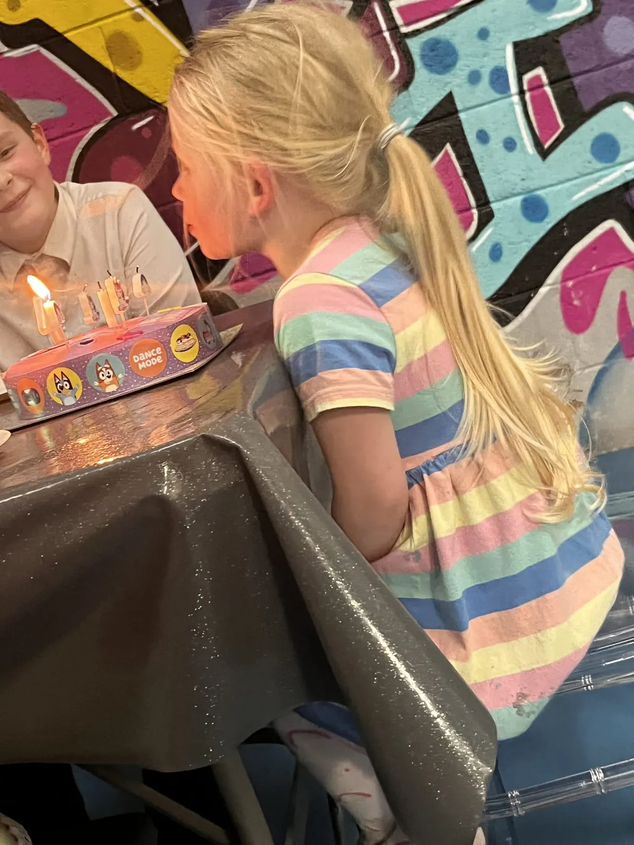 Young children celebrating a birthday with a cake and lit candles at an indoor play venue.