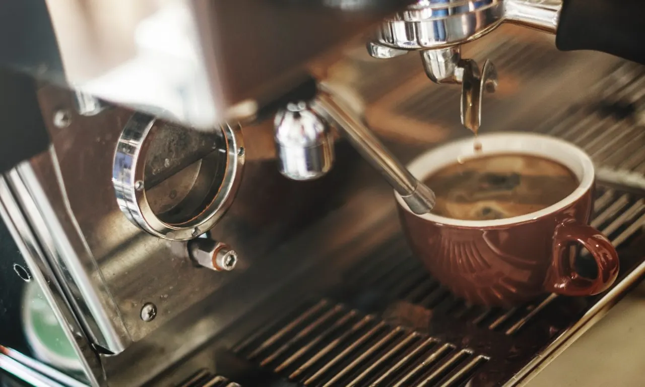 Espresso machine dispensing coffee into a brown ceramic cup on the group head.