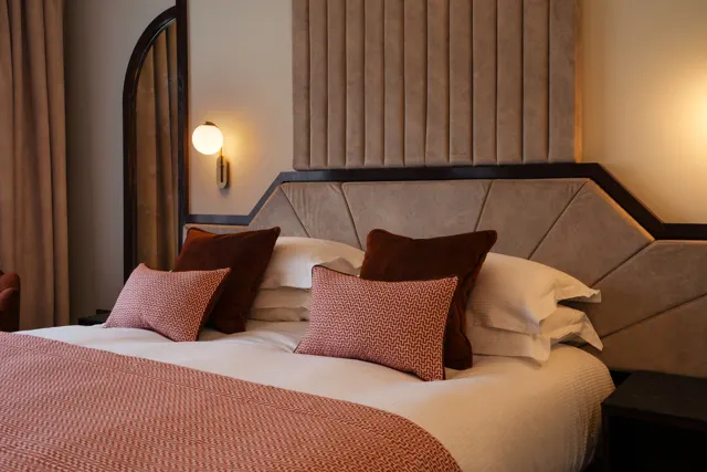 Modern hotel bedroom with double bed, decorative cushions, wall sconces and curtains.