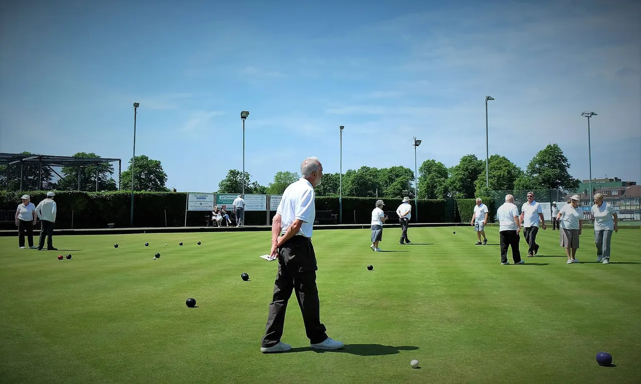 Multiple players enjoying bowls on a green outdoor grass pitch on a sunny day.